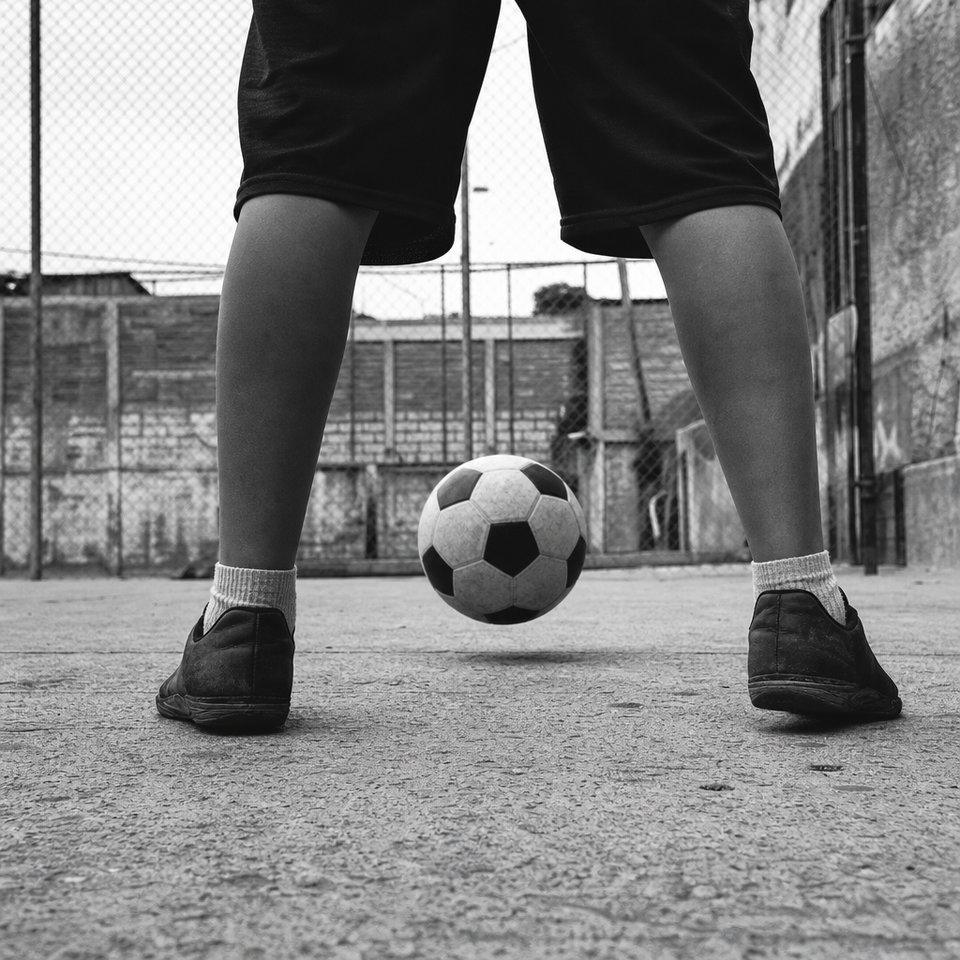 Vista a ras del suelo desde atrás de un jugador, con la pelota pasando por el hueco entre sus dos pies