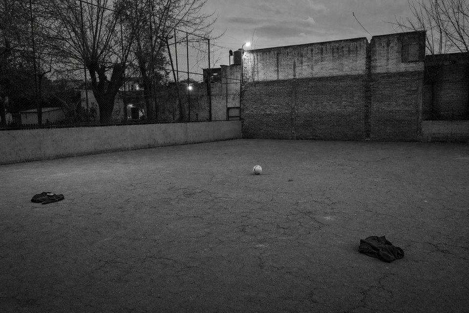 Cancha improvisada sobre asfalto agrietado, con dos camperas marcando un arco y una pelota en el centro
