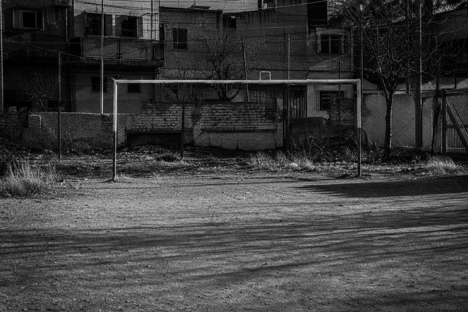 Terreno baldío de tierra apisonada usado como cancha, con un arco de dos caños sin red y un alambrado detrás