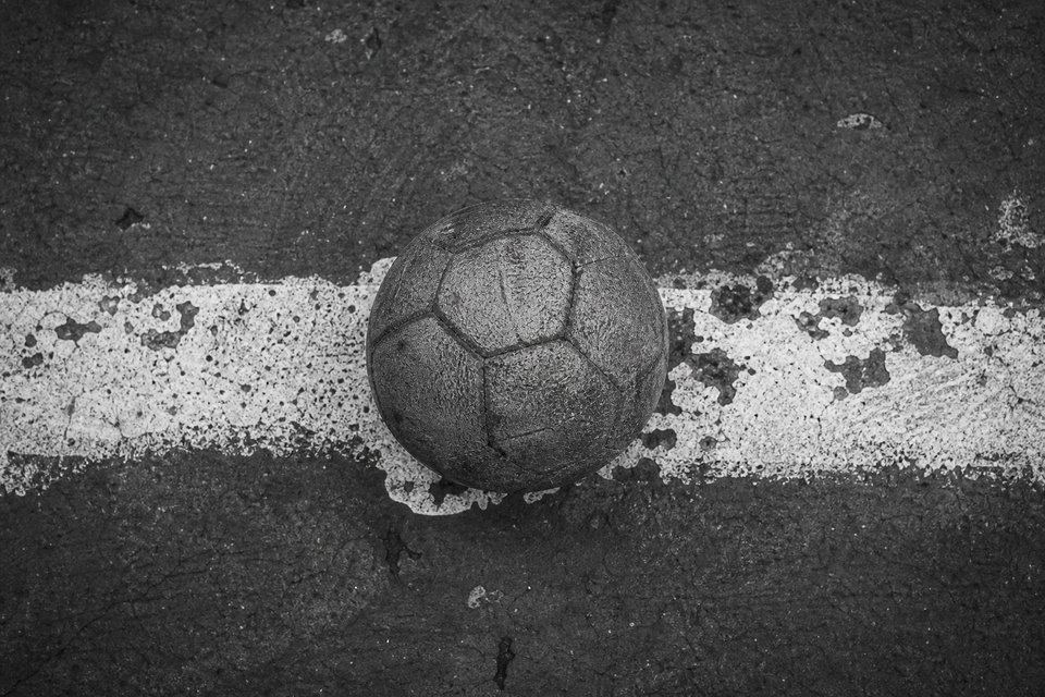 Pelota gastada apoyada sobre una línea blanca pintada a mano en el cemento, con la pintura saltada y repintada