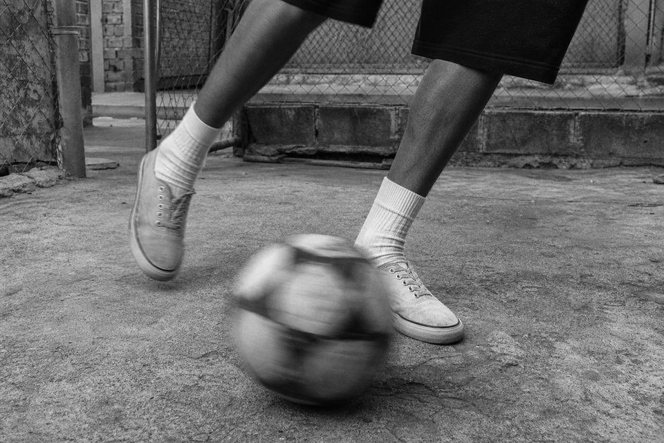 Primer plano de dos pies con zapatillas de lona controlando una pelota sobre cemento rugoso, con la pelota movida